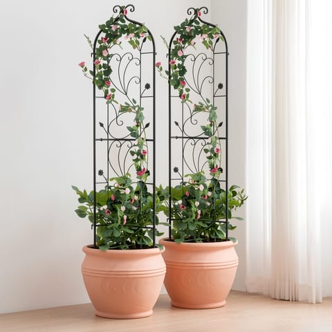 Two black metal garden trellises with pink roses and green leaves in terracotta pots on a beige surface