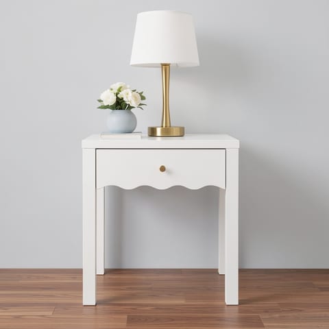 A white nightstand with a wavy apron design and a drawer, next to a bed with white linens.